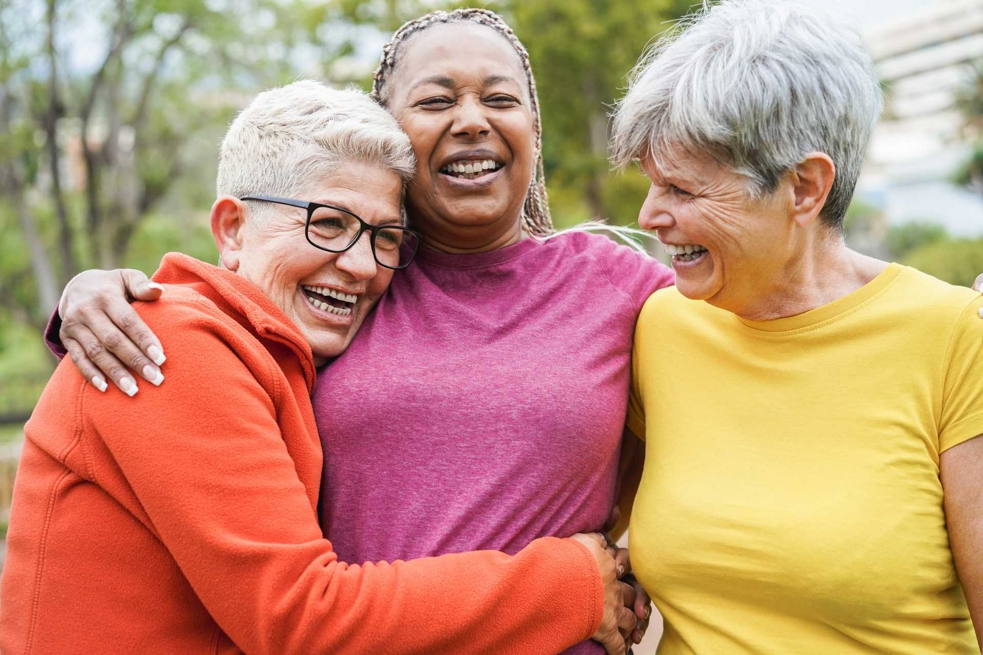 Three smiling women hugging each other outside, sharing a joyful moment together.